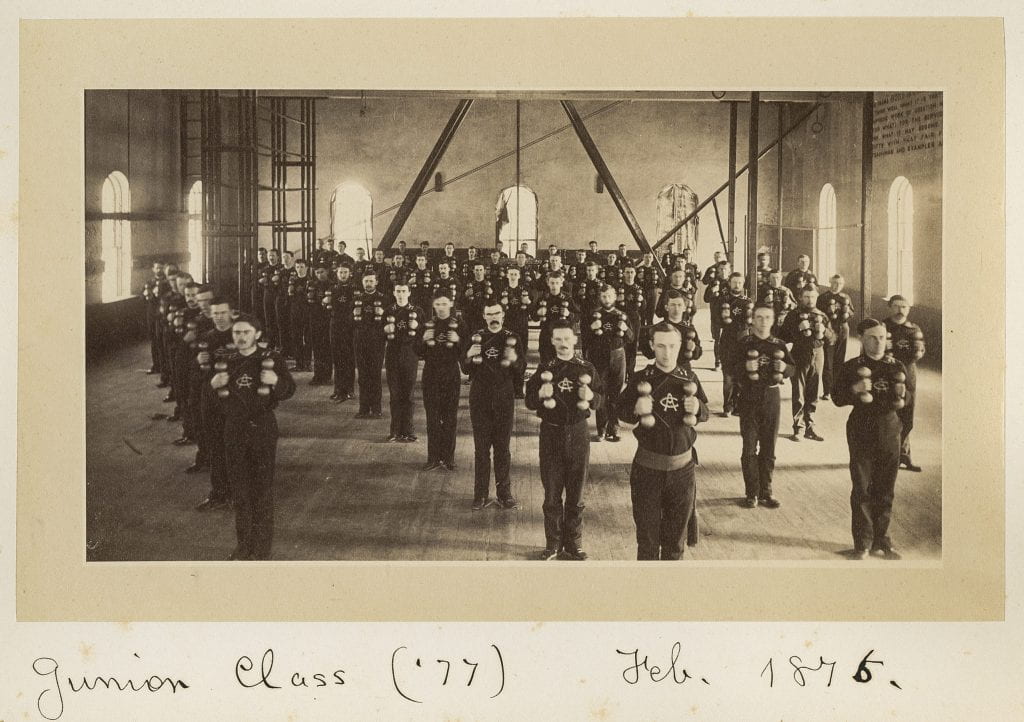 photograph showing the Class of 1877 in Barrett Gymnasium standing in formation holding dumbells