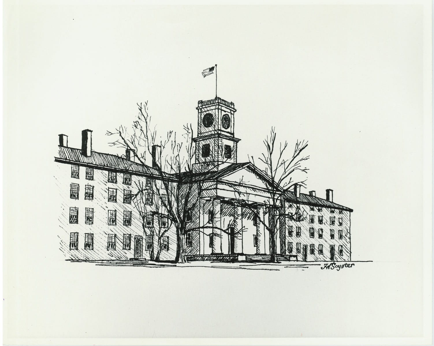 Two four-story brick building with chimneys stand on either side of a chapel fronted by columns. An American flag flies from the clock tower. The trees in front of the buildings are bare.