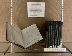 A series of plainly-bound books in a display case, one propped open to the title page