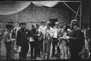 A black-and-white photograph of a group of men gathered around a microphone in the Coolidge Cage
