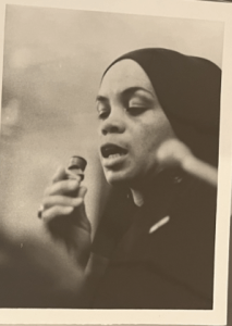 A black-and-white photograph of Sonia Sanchez speaking into a microphone