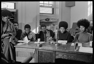 Six Black students sitting at a desk with notes and a microphone